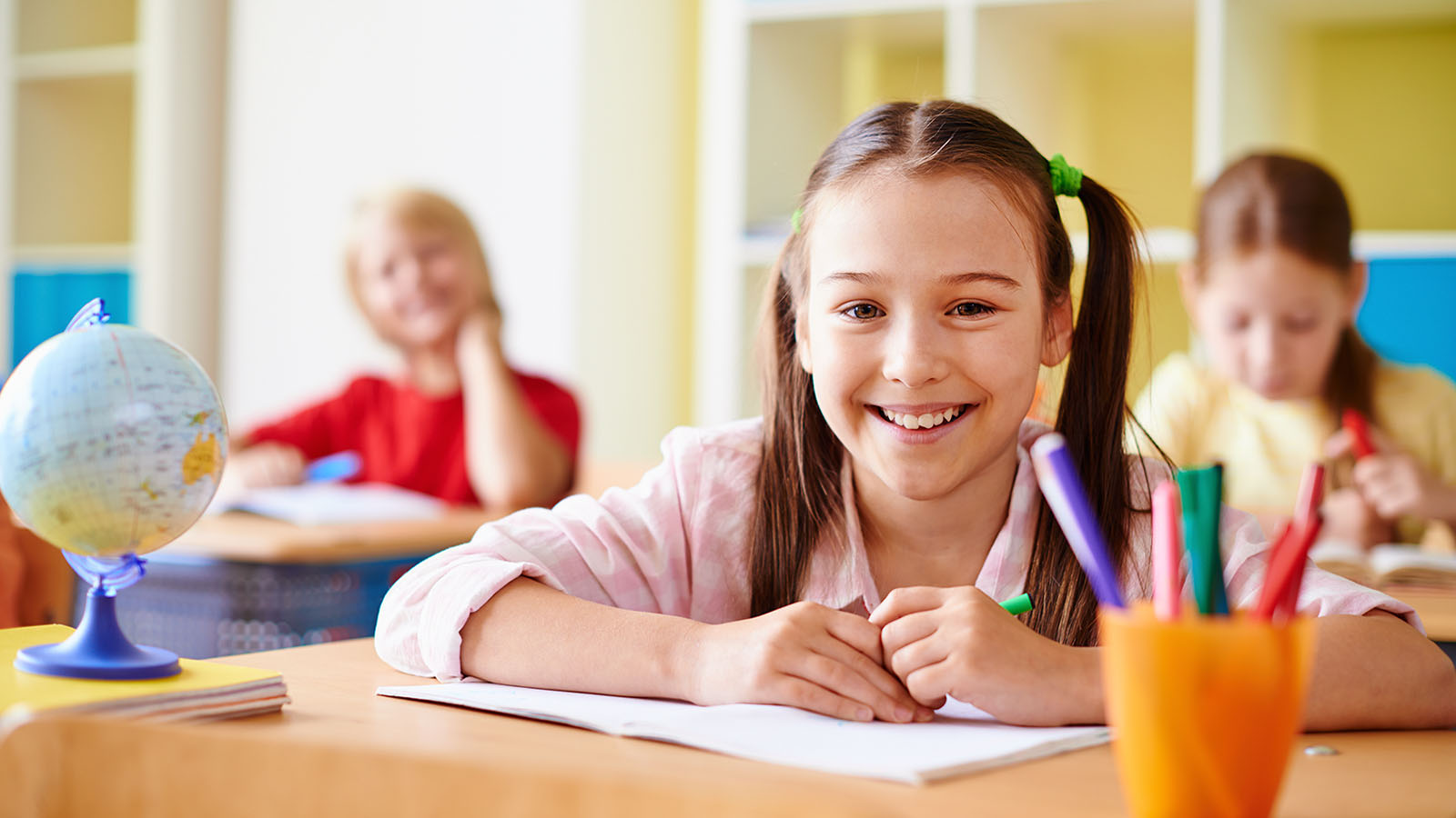 menina feliz em uma sala de aula, para representar o seguro acidentes pessoais escolar