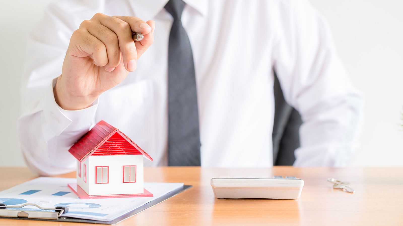 imagem close de um homem vestindo camisa social, em uma mesa com uma casa em miniatura, representando o seguro para imobiliária