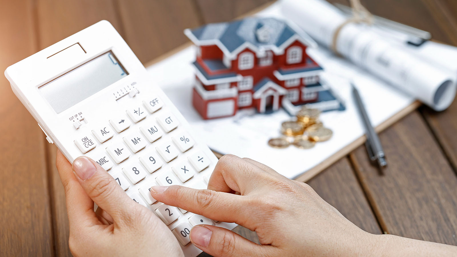 imagem com uma calculadora, uma casa em miniatura e outros papeis, representando o seguro fiança locatícia